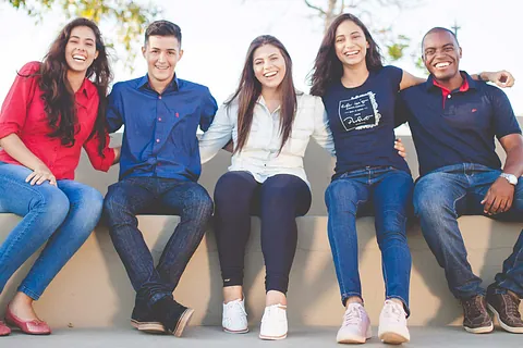 Diverse Gruppe lächelnder junger Erwachsener, die draußen zusammen sitzen.