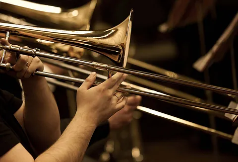 Nahaufnahme der Hände eines Musikers beim Spielen einer glänzenden Posaune aus Messing.