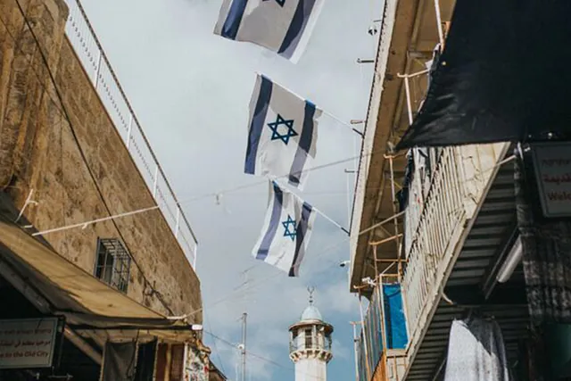 Israelische Flaggen zwischen Altstadtgebäuden mit einem Minarett.