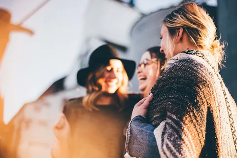 Drei Frauen lächeln und lachen gemeinsam im Freien.