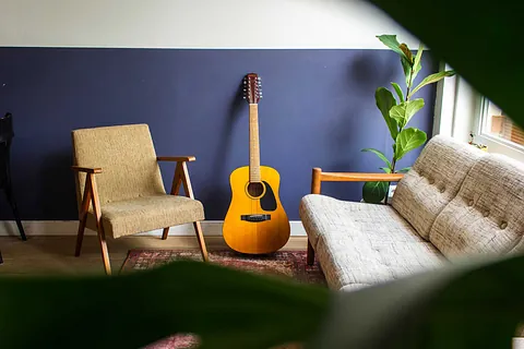 Akustikgitarre lehnt an einer lila Wand zwischen Sesseln.