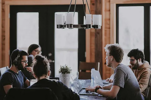 Eine Gruppe junger Menschen arbeitet gemeinsam an Laptops um einen Tisch.