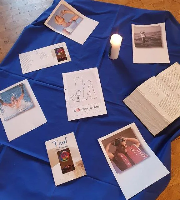 Informationsflyer, eine Kerze und ein geöffnetes Buch auf einem blauen Tuch.