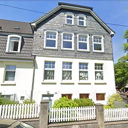 Traditionelles Haus mit schieferverkleidetem Obergeschoss und weißem Lattenzaun.