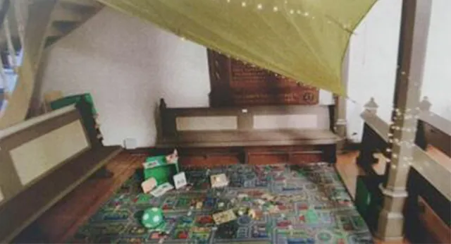 Kinderspielecke mit Teppich und Baldachin in einer Kirche.